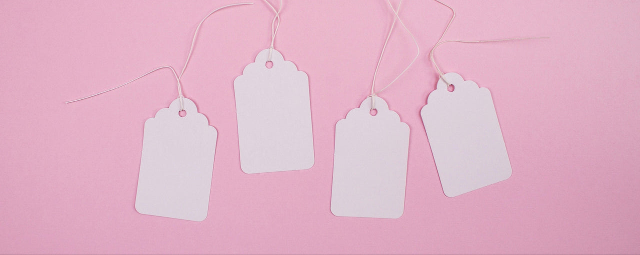Four white blank tags hanging on a string against a pink background
