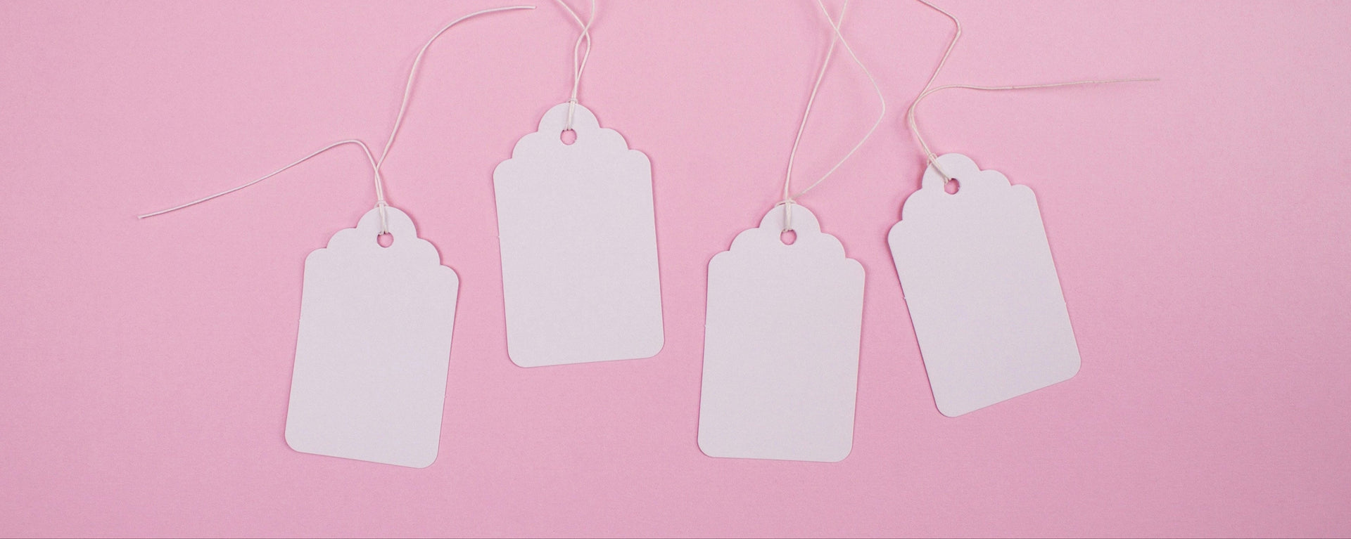 Four white blank tags hanging on a string against a pink background